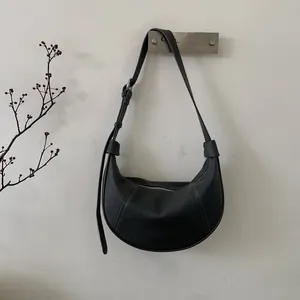 Detail of black litchi grain leather crescent bag with adjustable strap and silver buckle