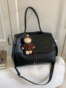 Schwarze Handtasche aus Lederimitat mit süßem Bärenanhänger auf weißem Polster