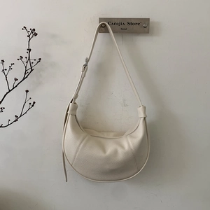 Macro detail of creamy white lychee grain leather on a minimalist crescent shoulder bag