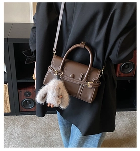 Close-up of brown crossbody bag with contrast stitching and plush rabbit keychain