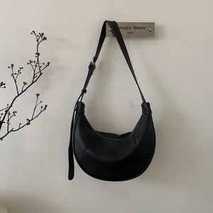 Detail of minimalist black litchi grain leather crescent bag with adjustable strap