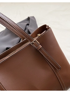 Close-up of brown leather tote bag with white contrast stitching and gold metal zipper