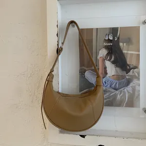 Detail view of a brown pebbled leather half-moon saddle bag hanging on a white wall
