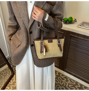 Détail du sac cabas plissé beige avec anses en cuir marron et pompons en perles colorées
