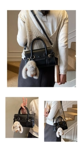 Detail of black leather handbag with white contrast stitching and a plush bunny charm