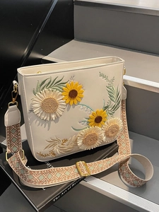 White faux leather shoulder bag with floral embroidery and wide geometric strap on steps