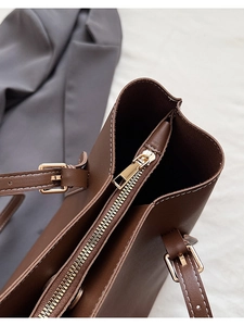 Detail view of brown tote bag with white contrast stitching and gold zipper closure