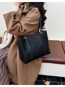Detail of black leather tote bag with white stitching worn by a model in autumn coat