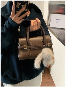 Close-up of dark brown leather handbag with white contrast stitching and plush rabbit charm