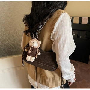 Detail of dark brown suede baguette bag with silver chain and cute bear charm