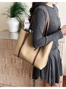 Detail of a large khaki tote bag with dark brown straps worn by a model in a modern setting