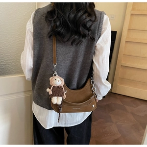 Detailed view of a brown hobo bag with a cute bear plush keychain and silver brand logo