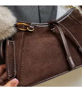 Macro shot of dark brown suede bag with white stitching and gold metal buckle detail