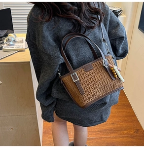 Détail d'un sac seau plissé marron foncé avec perles en bois et logo carré en métal
