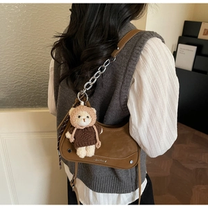 Detail of a brown leather crescent bag with silver chain and a cute teddy bear charm