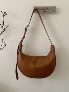 Brown leather croissant-style half-moon shoulder bag with adjustable strap in minimalist design
