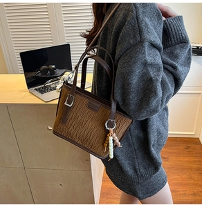 Texture détaillée du sac seau marron en cuir plissé avec boucle argentée et pendentif