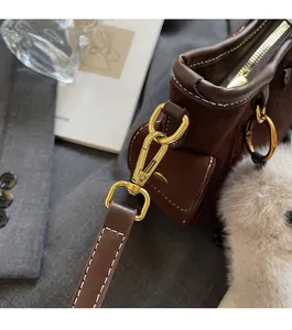 Detail of brown suede handbag with polished gold hardware and white contrast stitching
