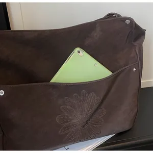 Detail of dark brown tote bag showing daisy embossing and large pocket for a tablet