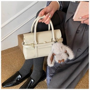 Detail of beige bowling bag with plush rabbit charm held by model in a grey suit