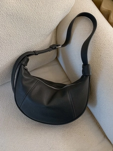 Minimalist black leather hobo shoulder bag with silver hardware on white textured sofa