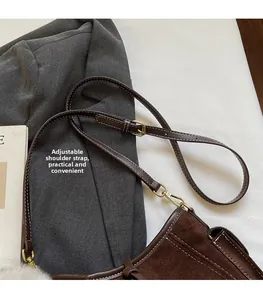 Detail of adjustable shoulder strap and retro gold hardware on dark brown suede crossbody bag