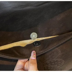 Detail of magnetic snap closure and embossed leather texture on dark brown bag