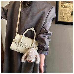 Detail of minimalist cream bowling bag with plush bunny charm and adjustable shoulder strap
