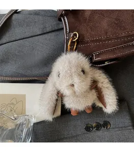 Close-up of a plush rabbit charm with grey fur and leather ears on a brown leather handbag