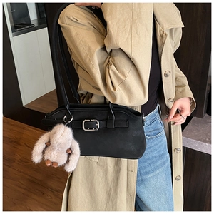 Détail d'un sac d'épaule noir mat avec œillets métalliques et breloque lapin en peluche