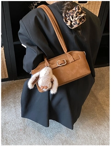 Détail d'un sac d'épaule en daim marron avec boucle métallique et breloque lapin en peluche