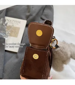Detail view of brown suede shoulder bag with magnetic clasp and plush ball accessory