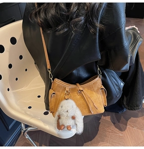 Detail of caramel suede shoulder bag with side flap pockets and plush bunny pendant