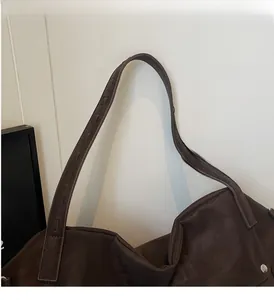 Detail of wide embossed shoulder strap and metal rivets on dark brown tote bag
