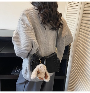 Detail of black faux suede shoulder bag with contrast stitching and plush rabbit charm