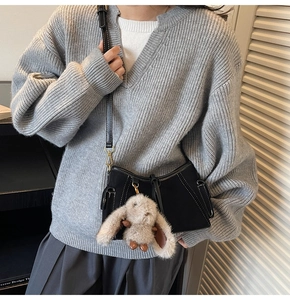 Close-up of black suede shoulder bag with white contrast stitching and bunny charm