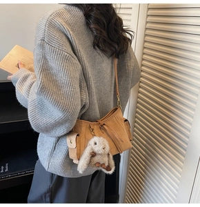 Detail of brown suede crossbody bag featuring side pocket, drawstring and bunny charm