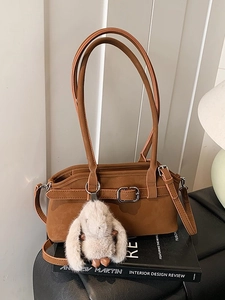 Sac bandoulière en cuir caramel avec pendentif lapin en peluche sur des livres noirs