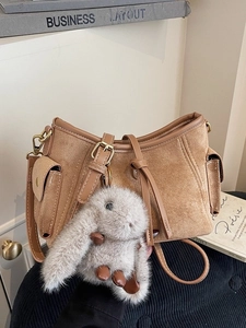 Brown suede shoulder bag with utility pockets and a plush rabbit charm in a cozy setting