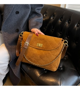 Detail of brown quilted suede crossbody bag with gold twist lock on black leather sofa