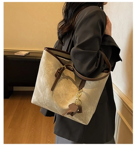 Detail of canvas tote bag with brown leather trim and elephant charm on model's shoulder