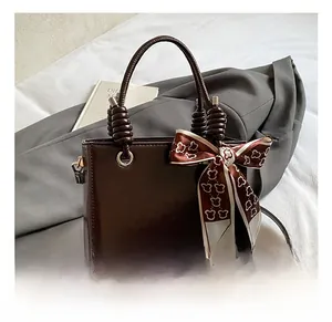 Detail of dark brown leather handbag with chic heart pattern silk scarf tied on handle