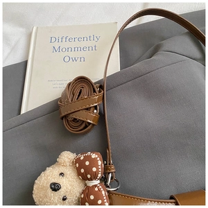 Brown leather crossbody bag with a cute plush bear pendant on a grey fabric background