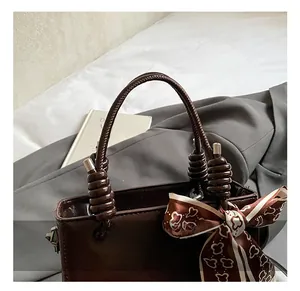 Detail view of smooth dark brown leather handbag with unique knotted handle and silk scarf