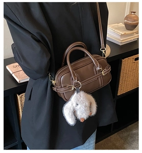 Detail showing deep brown Boston handbag with white contrast stitching and a plush rabbit charm