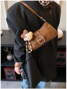 Detail of dark brown leather underarm bag with large gold buckle and cute bear pendant