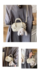 Close-up of cream Boston bag with dual buckles and a plush rabbit charm accessory