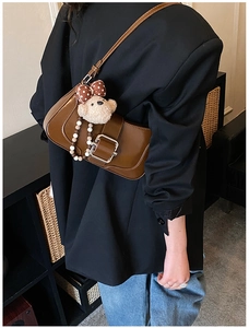 Detail of dark brown baguette bag with silver buckle and plush bear charm on a model