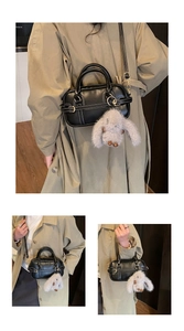 Detail of black PU Boston bag with white stitching, gold ring handle and plush rabbit charm
