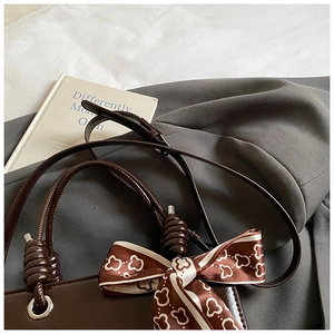 Detail of coffee brown glossy leather handbag with spiral handle and silk scarf decor